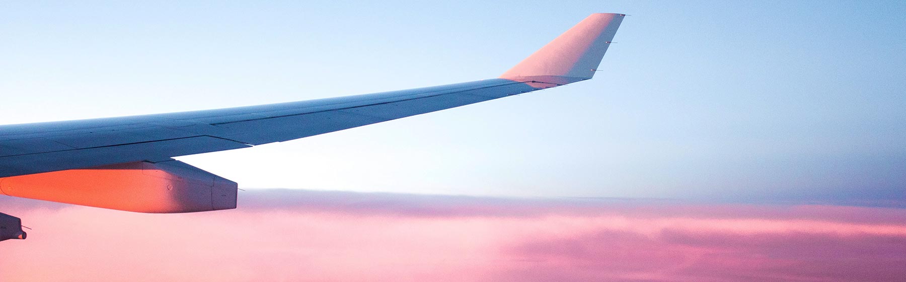 Airplane wings above the clouds at sunset - symbolic image for international patients traveling to Aschheim for treatment.